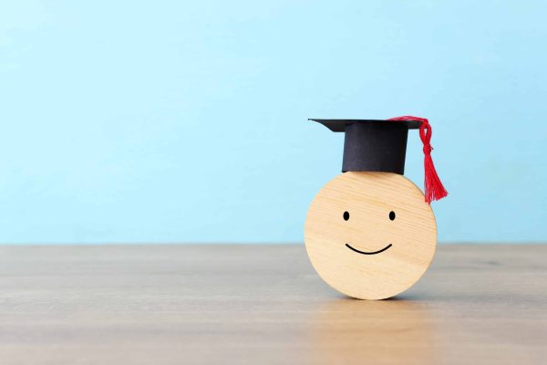 A,Smiling,Face,With,A,Graduation,Cap,On,Wooden,Cube.