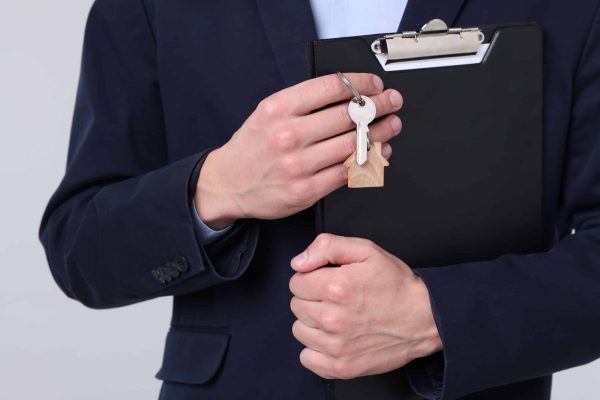 Real,Estate,Agent,Holding,Key,With,House,Shaped,Keychain,And